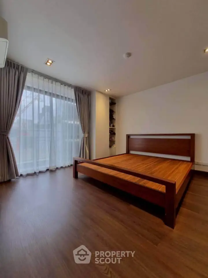 Spacious bedroom with wooden flooring and large window for natural light