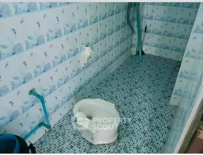 Unique bathroom with blue mosaic tiles and aquatic-themed wallpaper, featuring a traditional squat toilet.