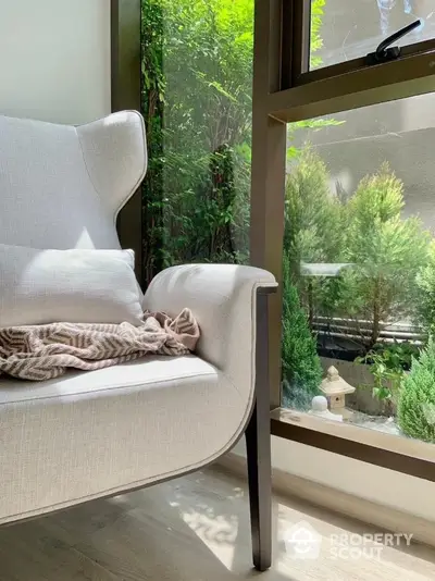 Cozy corner with elegant armchair and lush garden view through large window.