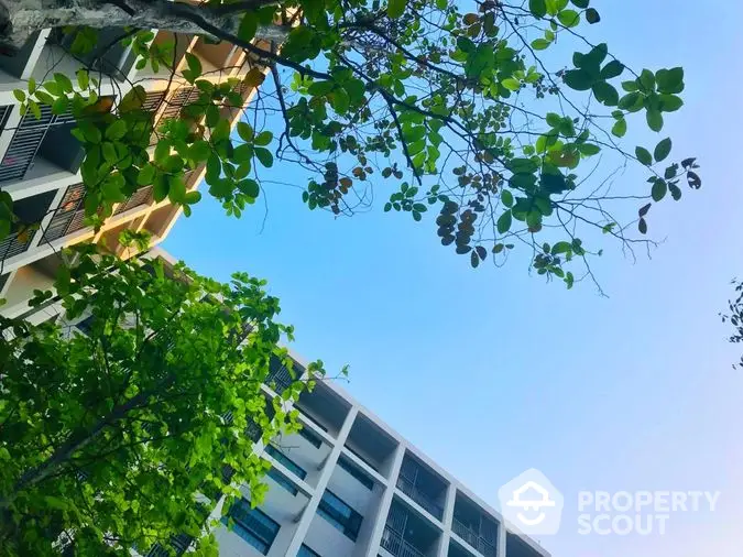 Serene urban oasis with lush greenery framing a modern apartment complex under a clear blue sky, perfect for eco-conscious city living.