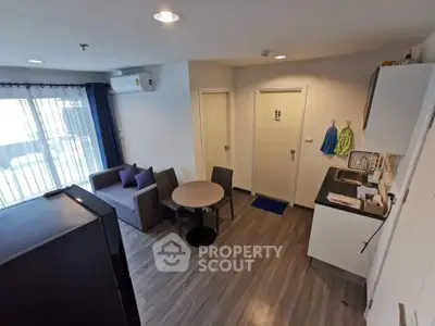 Modern compact living room with kitchenette and dining area, featuring sleek furniture and natural light.