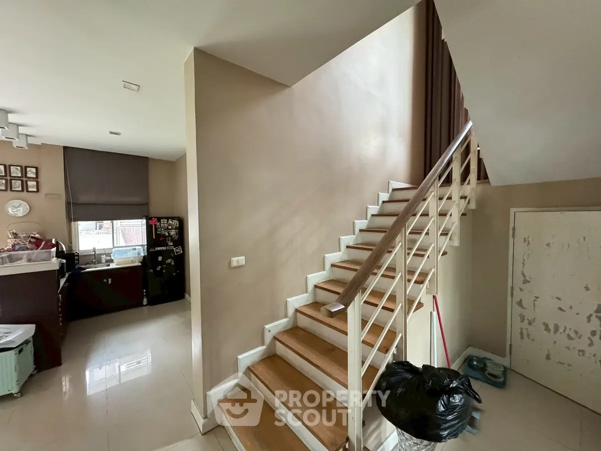 Modern home interior with wooden staircase and kitchen area, showcasing open layout design.