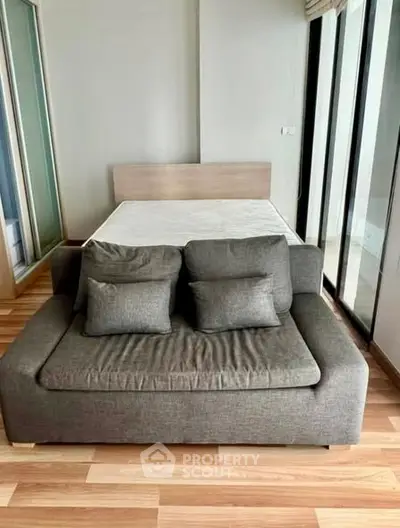 Modern studio apartment with stylish sofa and bed, featuring floor-to-ceiling windows for natural light.