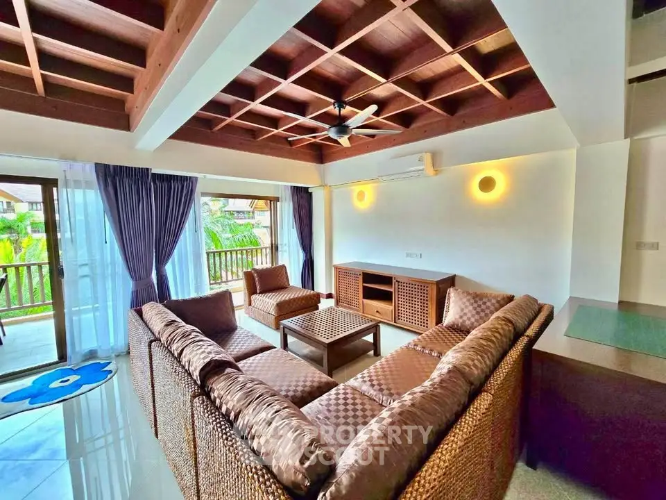 Spacious living room with elegant wooden ceiling and large windows opening to a balcony with lush views.