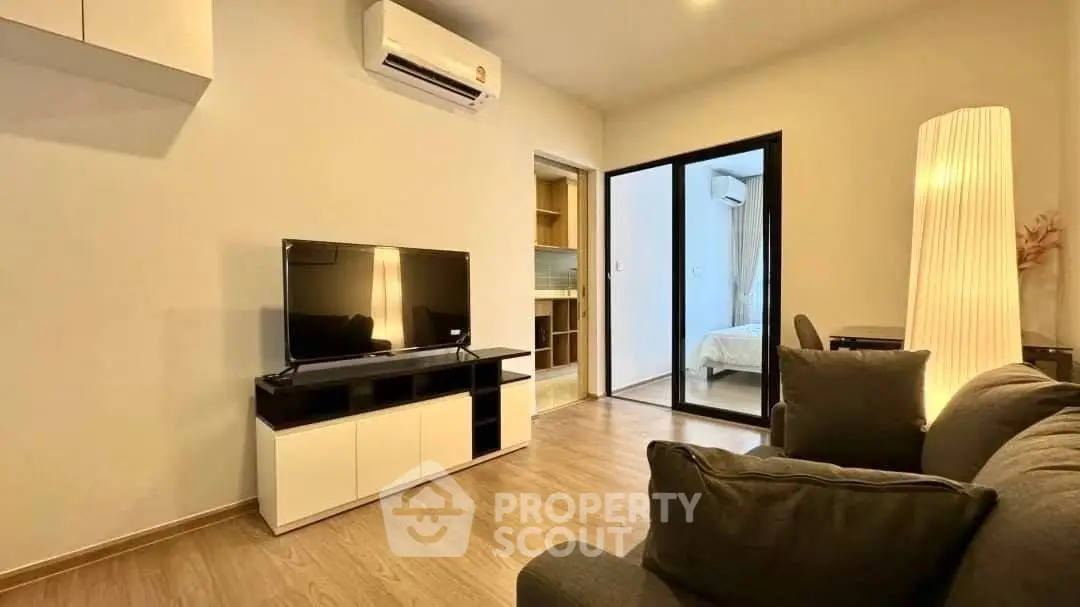 Modern living room with sleek TV setup and cozy seating, leading to a bedroom with stylish decor.
