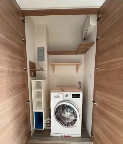 Compact laundry area with Bosch washing machine and wooden shelves in modern apartment.