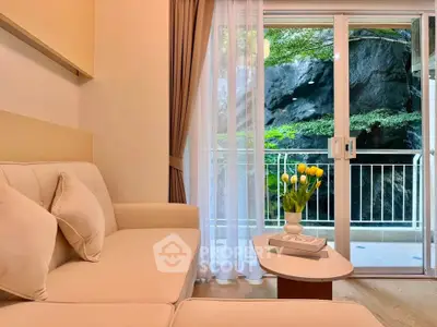 Cozy living room with beige sofa and balcony view of lush greenery