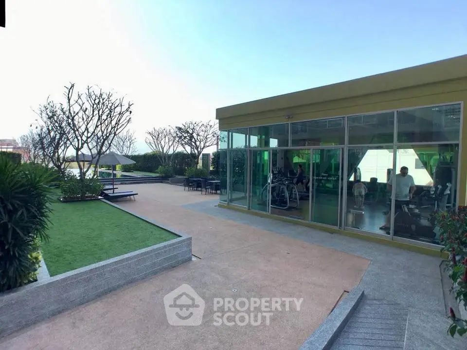 Modern rooftop gym with glass walls and outdoor garden area.