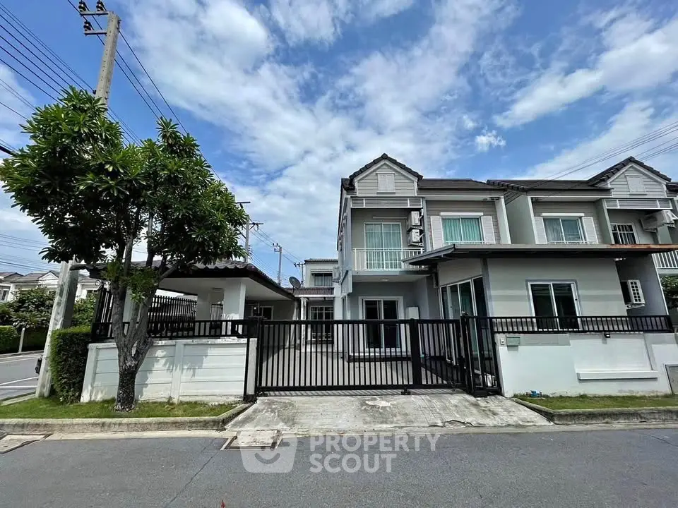 Charming suburban house with gated entrance and lush greenery under a bright blue sky.