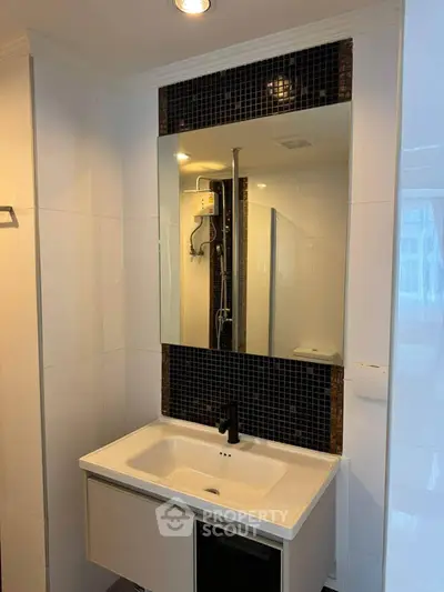 Modern bathroom with sleek vanity and large mirror, featuring elegant black tile accents and contemporary fixtures.