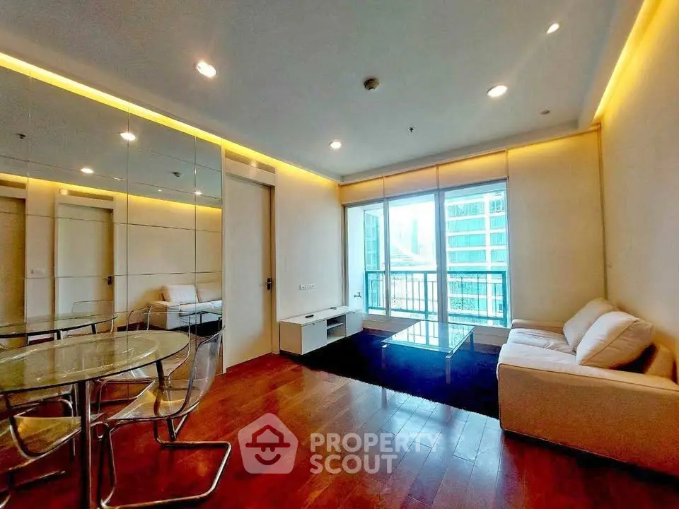 Modern living room with floor-to-ceiling windows and city view, featuring sleek furniture and wooden flooring.