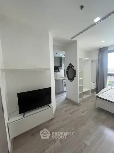 Modern studio apartment with sleek design, featuring a cozy bed, TV, and open kitchen layout.