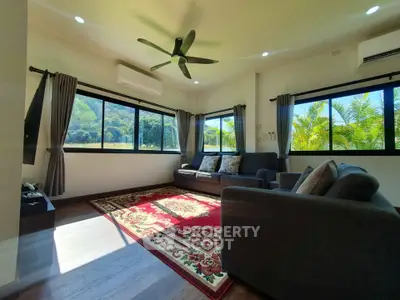 Spacious living room with large windows and scenic views, featuring modern furniture and a ceiling fan.