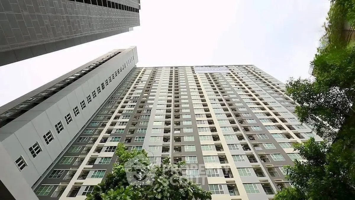 Modern high-rise apartment building with lush greenery and clear sky view.