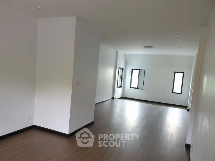 Spacious empty room with wooden flooring and natural light from windows.