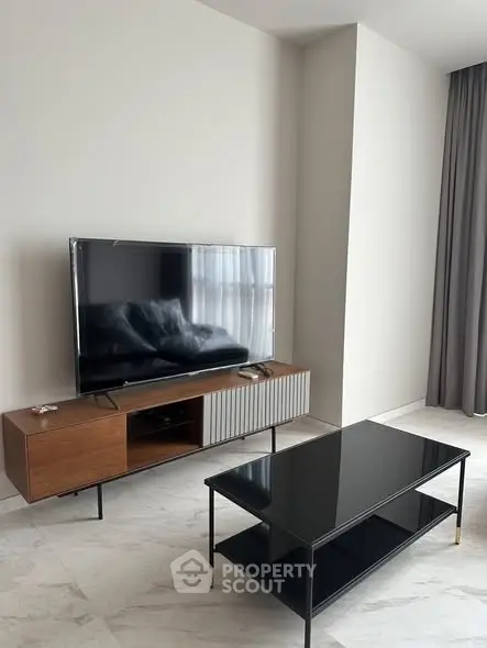 Modern living room with sleek TV stand and glass coffee table on marble floor.