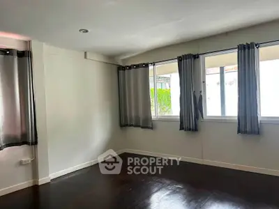 Spacious empty room with dark wood flooring and large windows for natural light.