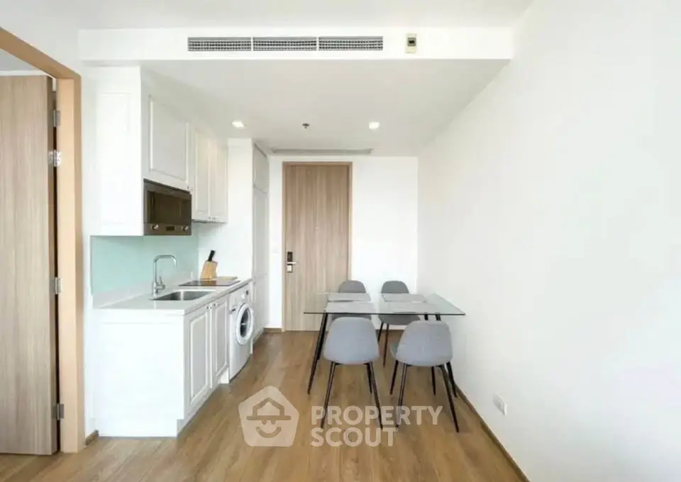 Modern apartment kitchen with dining area, featuring sleek white cabinetry and integrated appliances.