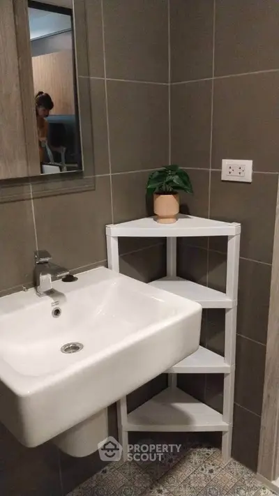 Modern bathroom with sleek sink and corner shelf, featuring stylish tile flooring and neutral wall tones.