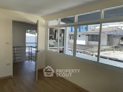 Spacious and sunlit living room with large windows and balcony access, featuring hardwood floors and a modern, airy ambiance.