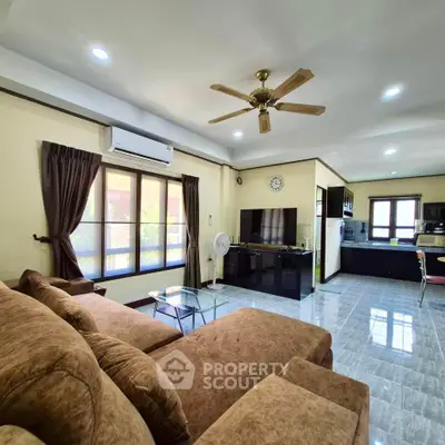 Spacious living room with modern decor and open kitchen layout, featuring a cozy sofa and ceiling fan.