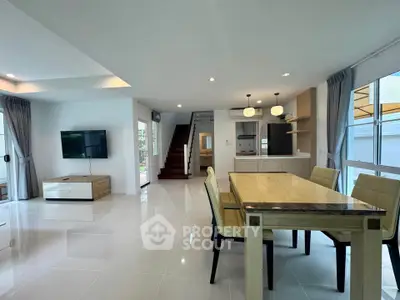 Spacious modern living room with dining area and staircase, featuring sleek furniture and ample natural light.