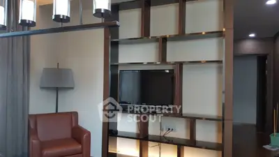 Modern living room with stylish shelving and flat-screen TV, featuring elegant lighting and a comfortable leather chair.