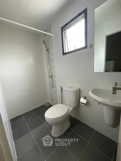 Modern bathroom with sleek fixtures and tiled walls, featuring a shower and window for natural light.