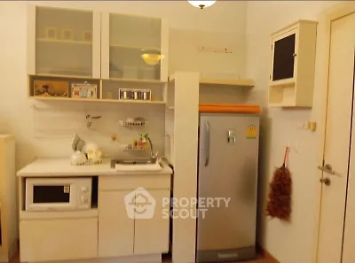 Compact kitchen with fridge, microwave, and storage cabinets in cozy apartment.