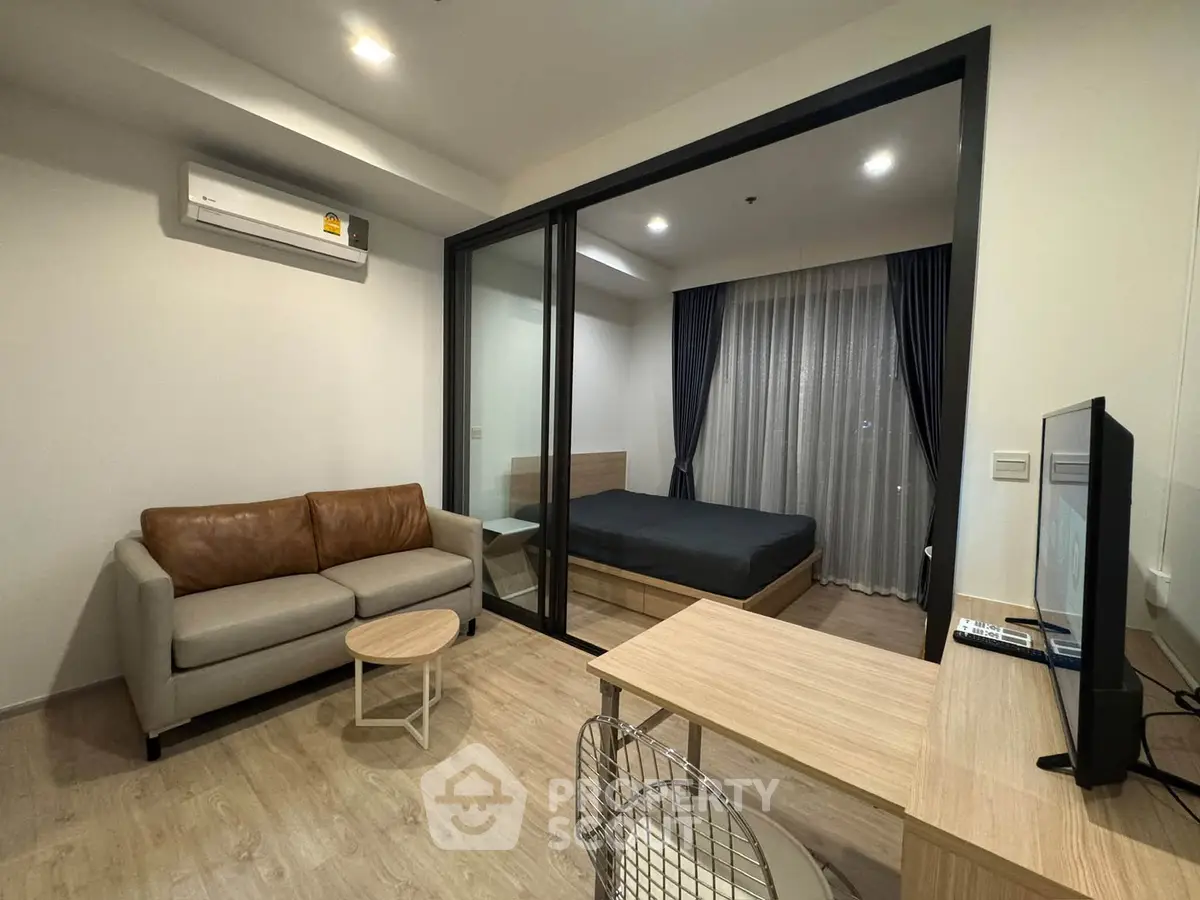 Modern studio apartment with glass partition, cozy living area, and sleek furnishings.