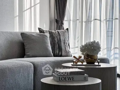 Elegant living room with modern sofa, stylish decor, and natural light through sheer curtains.