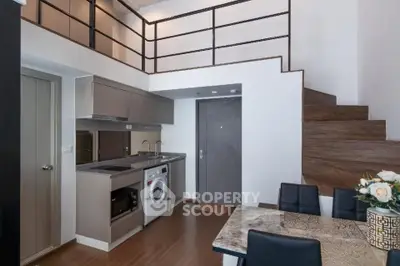 Modern loft apartment with open kitchen and stylish dining area, featuring a washing machine and wooden staircase.