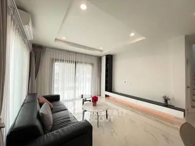 Modern living room with sleek black sofa and elegant decor, featuring large windows and natural light.