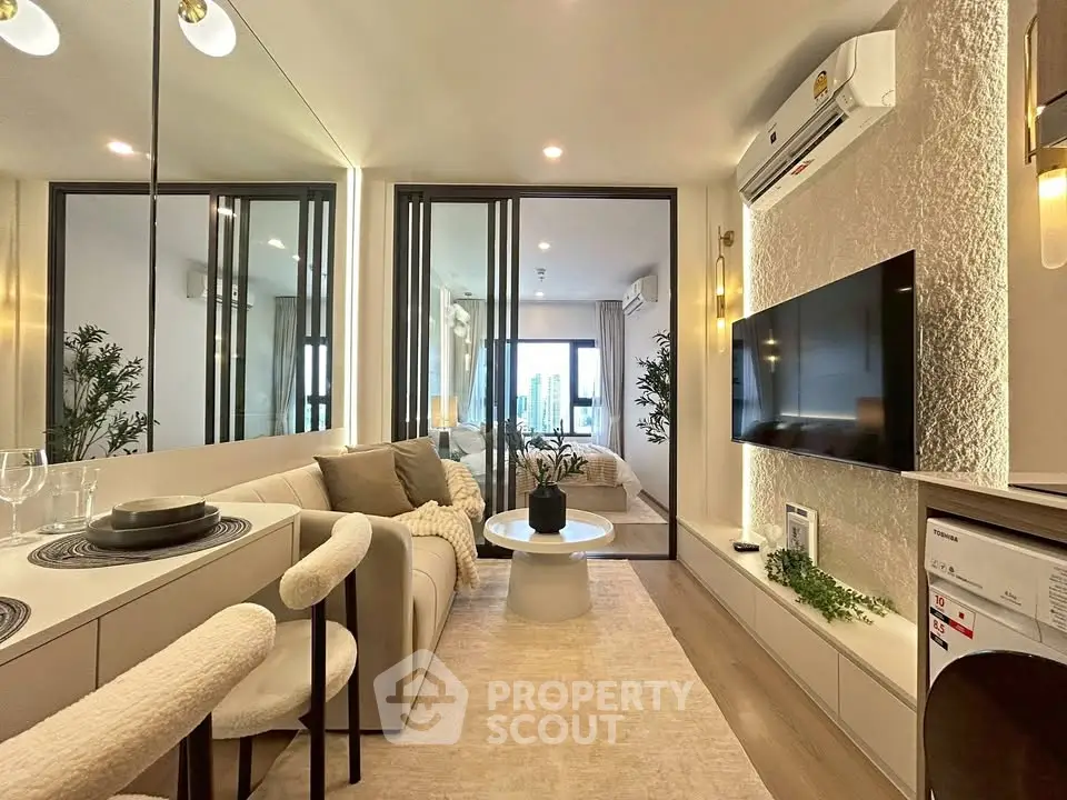 Modern living room with stylish decor and open layout leading to a cozy bedroom, featuring a wall-mounted TV and elegant furnishings.