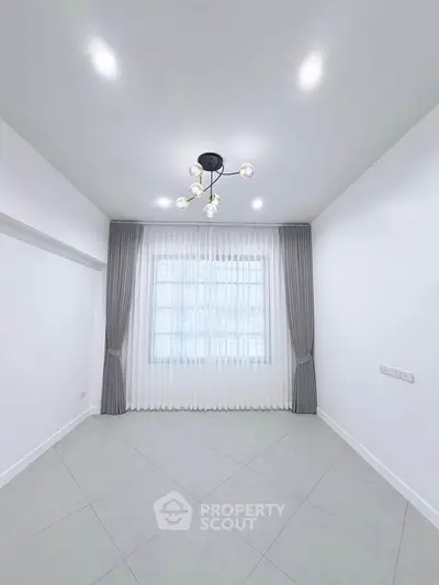 Spacious empty room with modern chandelier and large window, perfect for customization.