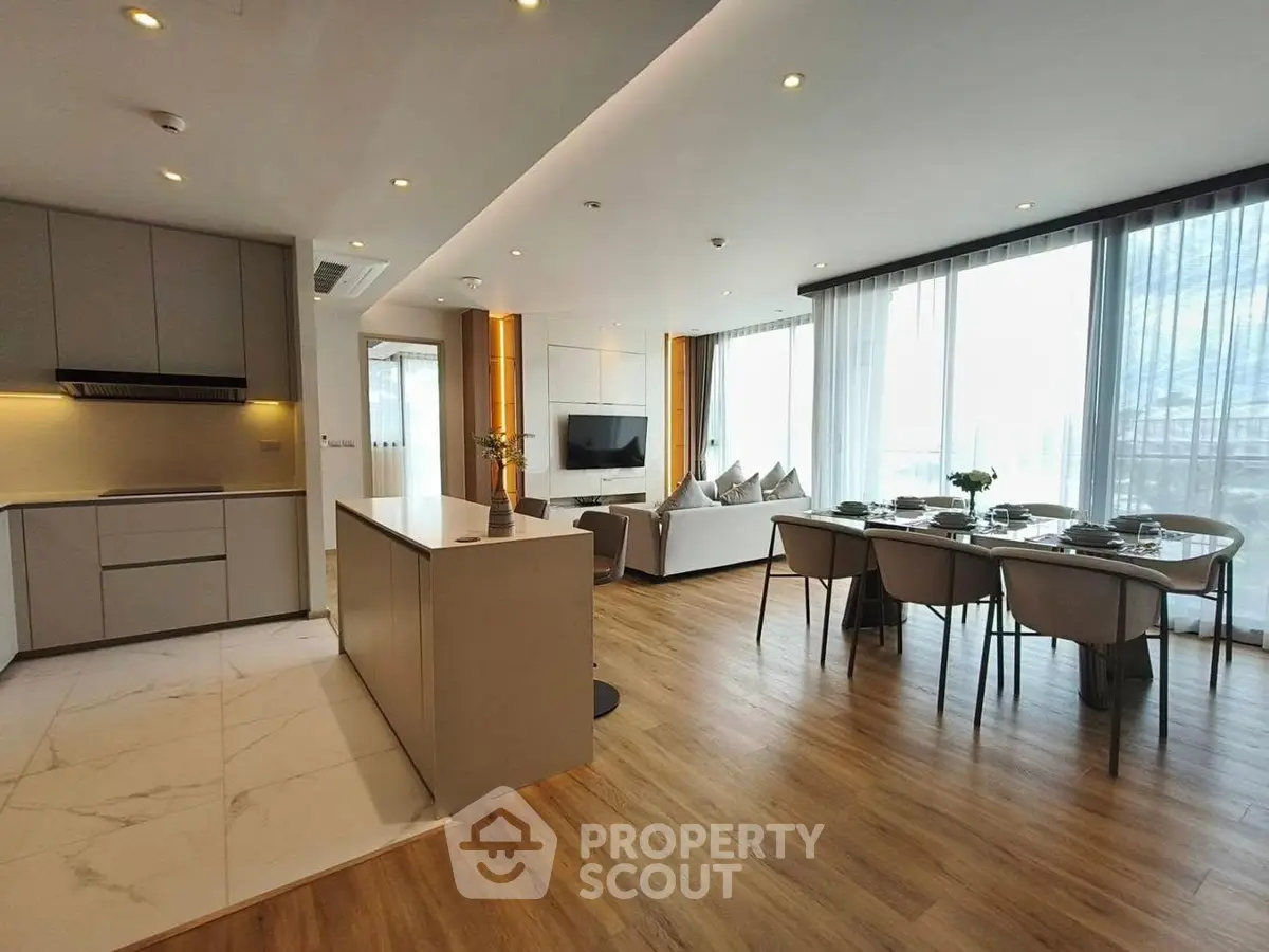 Modern open-plan living room and kitchen with elegant dining area and large windows.