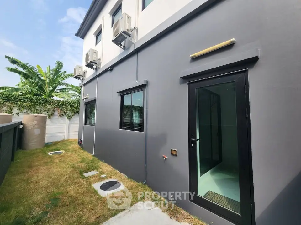 Modern exterior view of a house with air conditioning units and a small garden area.