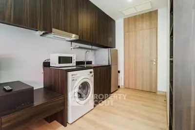Modern kitchen with washing machine and microwave in sleek wood cabinetry.