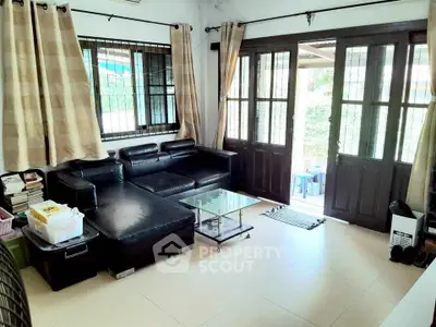 Cozy living room with black leather sofa and glass coffee table, natural light from large windows.