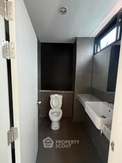 Modern bathroom with sleek design and dark tiles, featuring a toilet and a wall-mounted sink.