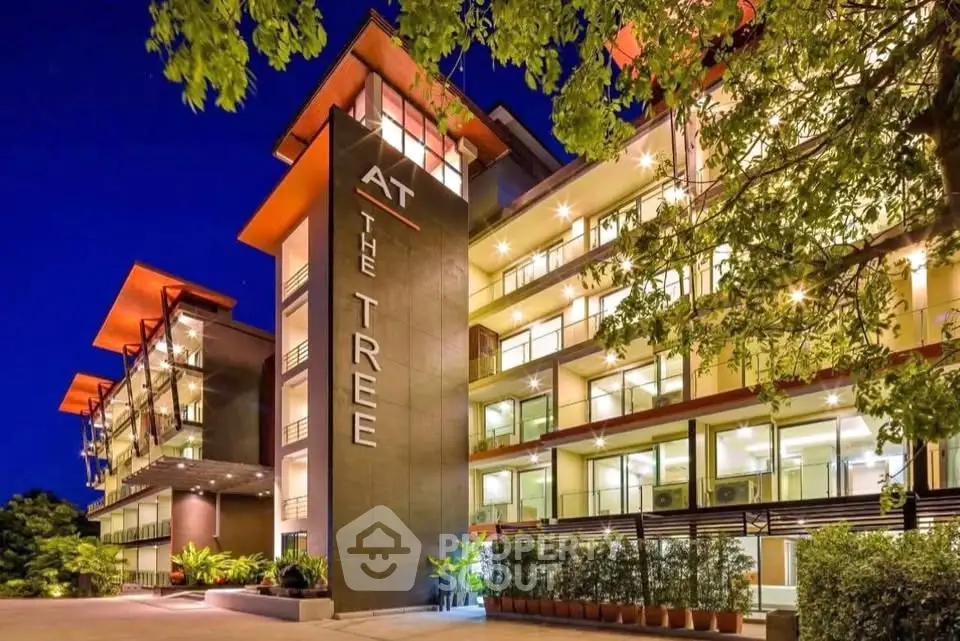 Modern apartment building with illuminated balconies and lush greenery at night.