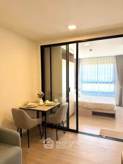 Modern apartment with open layout, featuring a cozy dining area and a bedroom separated by glass sliding doors.