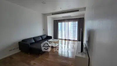 Spacious modern living room with sleek black sofa and large window offering city views.