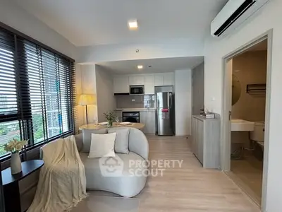 Modern open-plan living room with kitchen, featuring sleek furniture and large windows.