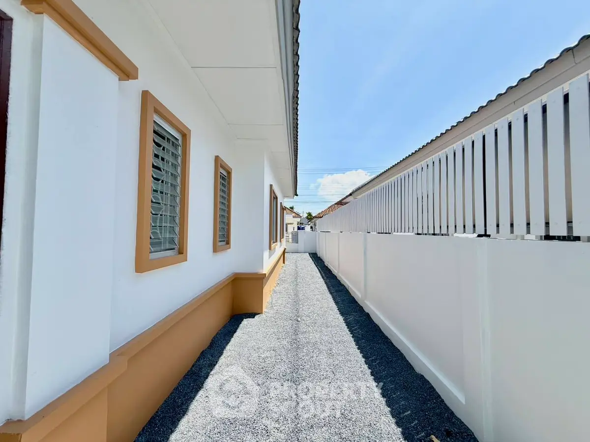 Modern exterior walkway with white walls and gravel path in sunny residential area.