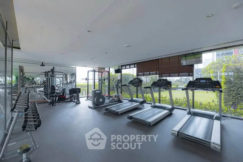 Spacious modern gym with treadmills and weight equipment, overlooking lush greenery.