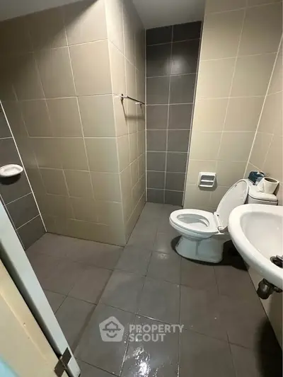 Modern bathroom with tiled walls and floor, featuring a toilet and sink.