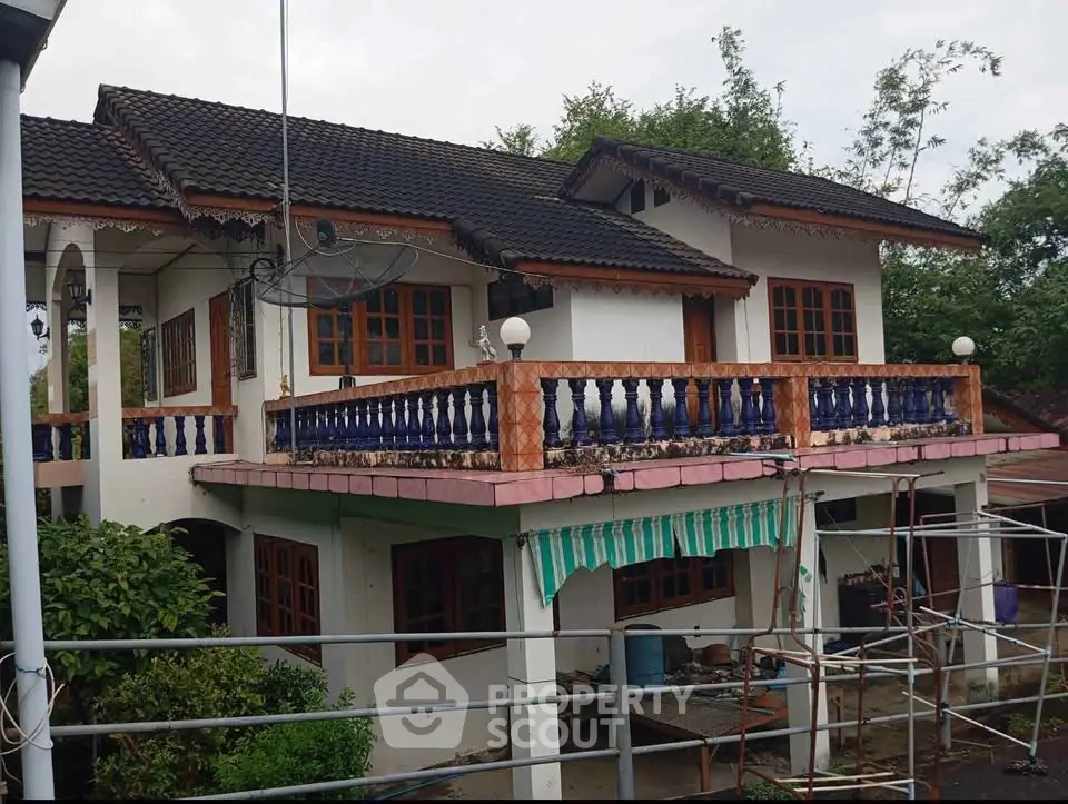Charming two-story house with traditional design and spacious balcony, surrounded by lush greenery.