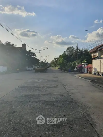 Quiet residential street with clear sky and distant airplane, perfect for peaceful living.