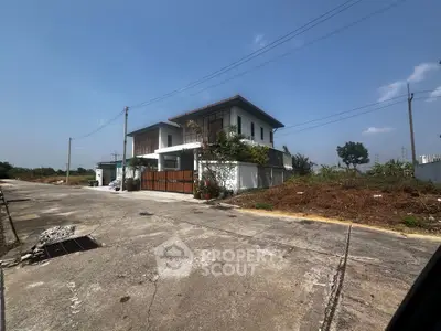 Modern two-story house with spacious driveway and lush greenery under clear blue sky.